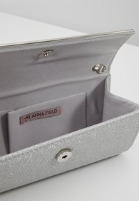 Pochette paillettes argentée ouverte, dévoilant un intérieur en tissu avec fermeture à pression magnétique et petite poche intérieure avec étiquette Anna Field.