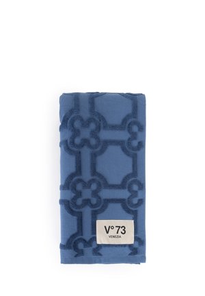 Blue folded towel with raised geometric pattern and a white label reading "V°73 VENEZIA" on a white background.