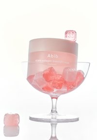 Maschera notte Abib PDRN collagen in un contenitore rosa traslucido, all'interno di un bicchiere trasparente con cubetti gelatinosi rosa e bianchi.