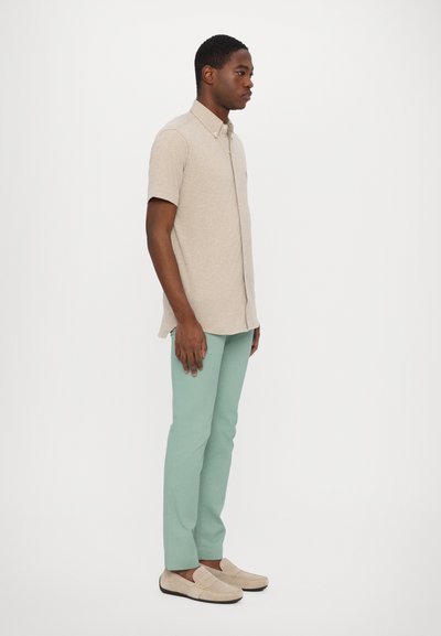 Camisa beige de manga corta con botones, pantalones verde menta y mocasines beige claros. Textura suave, diseño ajustado, silueta relajada.