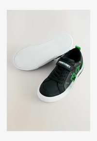 Zapatillas negras con superficie texturizada, suela blanca, acentos pixelados verdes y una correa con la marca "Minecraft".