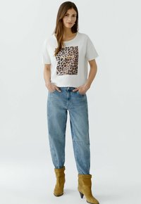 T-shirt blanc à manches courtes avec un motif carré en imprimé léopard, associé à un jean baggy bleu clair et des bottines en cuir beige.