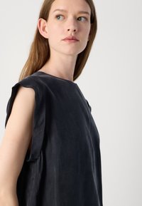 Top nero senza maniche con scollatura tonda, realizzato in tessuto morbido. Presenta cuciture per le spalle morbide e arrotondate e una vestibilità rilassata.
