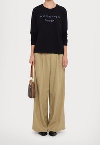 Maglietta nera a maniche lunghe con lettering decorato, abbinata a pantaloni beige larghi. Porta una piccola borsa marrone con tracolla.