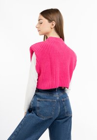 Roze gebreide croptop met een hoge halslijn en zonder mouwen, gecombineerd met blauwe high-waisted spijkerbroek. Glad oppervlak en ribbelpatroon.