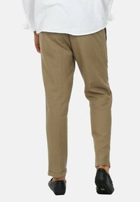 Pantaloni beige su misura realizzati in un tessuto leggero, con una vestibilità slim, orli alla caviglia e indossati con scarpe slip-on nere.