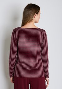 Burgundin pitkähihaista paitaa, jossa on kapeat valkoiset raidat, veneellinen pääntie ja kapea silhouette. Pehmeä kangas, jossa on hieman venyvyyttä.