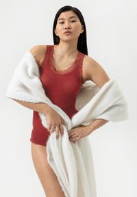 Un body rouge à côtes avec une bordure en dentelle, associé à un doux châle blanc. Le modèle pose avec le châle drapé autour d'elle.