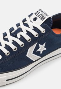 Marina canvas sneakers med vit snörning, med stjärnlogotyp och grå v-formad detalj. Gummisula med svart och vit rand.