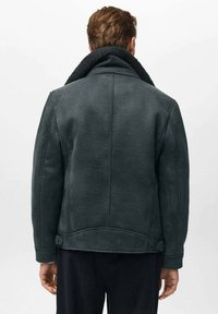 Giacca in shearling grigio scuro con un ampio colletto e un interno testurizzato. Presenta bottoni laterali e una silhouette snella.