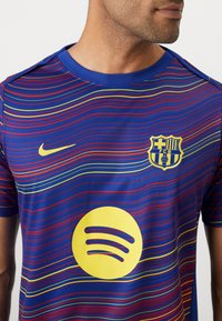 Nike Barcelona-tröja med färgglada vågmönster i blått, rött och gult. Innehåller Spotify-logotyp i fet gult och klubbens märke.
