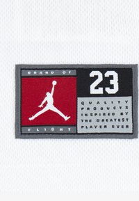 Vävd emblem med en vit Jumpman-logotyp på röd bakgrund med grå kant. Texten inkluderar "BRAND OF FLIGHT" och "23" i svart och vitt.