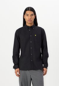 Camicia nera a maniche lunghe con colletto button-down, tasca sul lato sinistro del petto, con un piccolo logo ricamato giallo e bottoni blu.