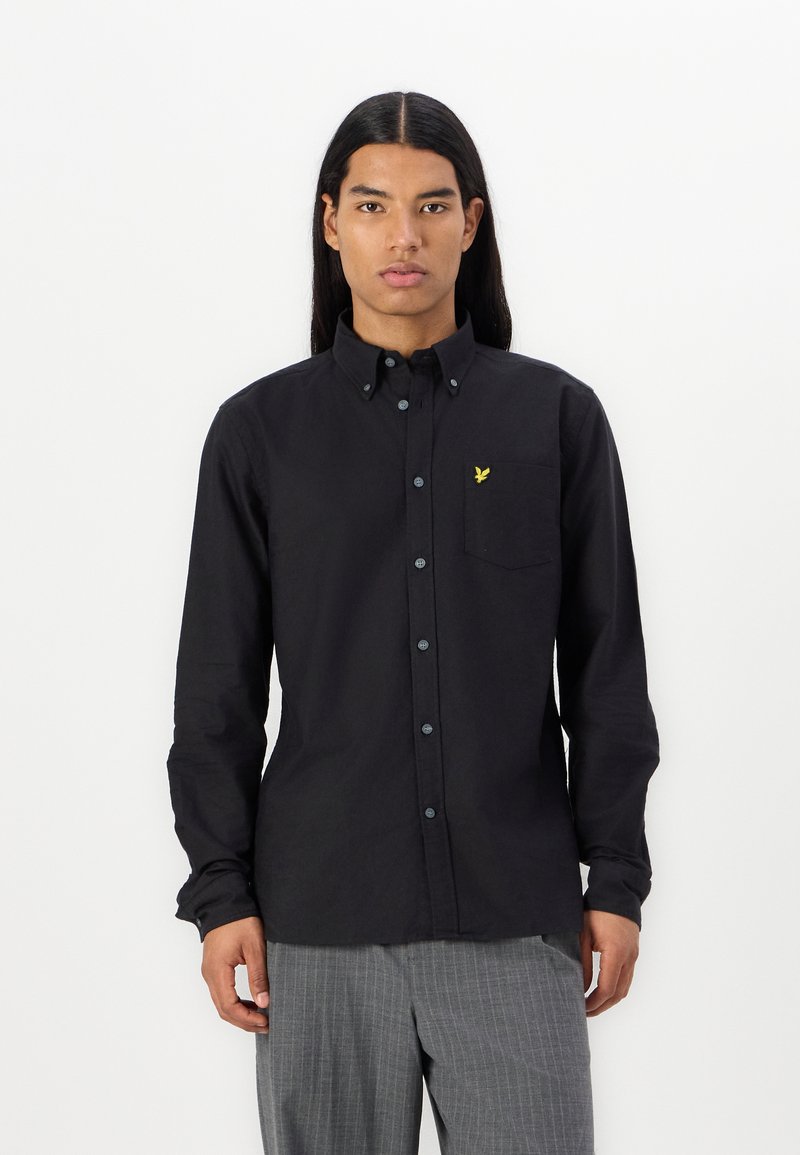 Camicia nera a maniche lunghe con colletto button-down, tasca sul lato sinistro del petto, con un piccolo logo ricamato giallo e bottoni blu.