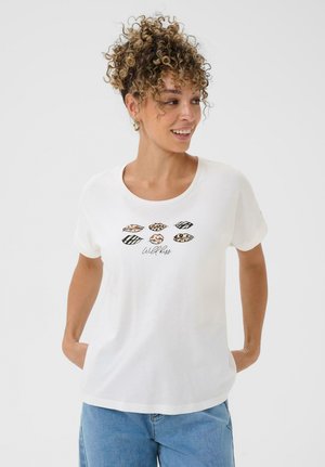 Woman with curly hair wearing a white T-shirt printed with six animal-patterned lips and "Wild kiss" text, paired with blue jeans.