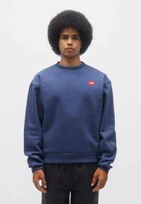Sudadera azul marino hecha de una tela suave, con un cuello redondo y puños acanalados; pequeño logotipo rojo en el pecho.
