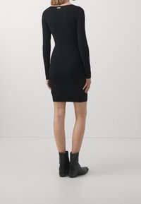 Abito nero a coste con maniche lunghe, silhouette aderente e scollatura a barca. Abbinato a stivaletti neri alla caviglia. Design minimalista.