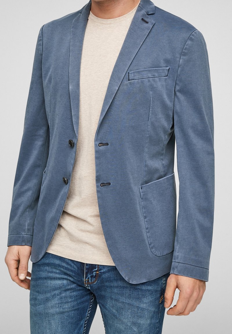 Marynarka w jasnoniebieskim połączeniu bawełny, dopasowany krój, jednorzędowa z dwoma czarnymi guzikami, klapy w kształcie litery notched i jedna kieszeń na piersi. Połączona z beżowym T-shirtem.