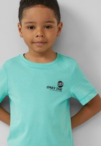 Turkoois katoenen t-shirt met korte mouwen, voorzien van een zwart gedrukt tekst en logo op de linkerkant van de borst. Glad textuur, reguliere pasvorm.