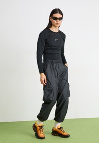 Black long-sleeve athletic shirt with Nike logo, paired with black cargo pants and orange sporty sneakers. Smooth and sleek texture throughout.