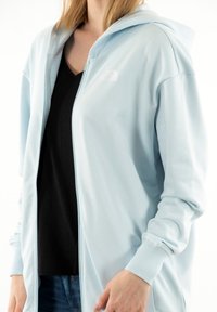 Felpa zip blu chiaro realizzata in morbido tessuto, con cerniera frontale, polsini a coste e logo del marchio sul lato sinistro del petto.