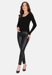 Schwarzes geripptes Langarmoberteil mit Rundhalsausschnitt, kombiniert mit hoch waisted schwarzen Skinny-Hosen aus Kunstleder und schwarzen High Heels.
