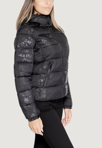 Giacca a vento nera con design trapuntato, tasche con zip e stampe grafiche. La giacca presenta un colletto alto e polsini elasticizzati.