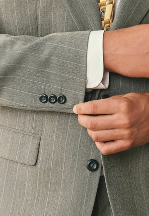 Hands adjusting the cuff of a gray pinstripe suit jacket over a white shirt and patterned tie.