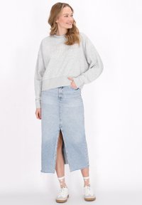 Felpa grigia corta con scollatura rotonda abbinata a una gonna maxi in denim azzurro chiaro con spacco anteriore, indossata con sneakers bianche.