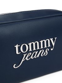 Pieni navy sininen keinonahkainen pussi, jossa on hopeanhohtoinen logo "tommy jeans". Varustettu vetoketjukiinnityksellä ja teksturoiduilla pinnan yksityiskohdilla.