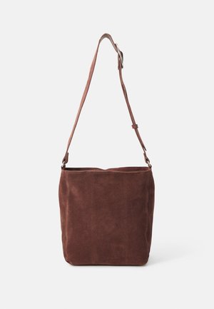 Brązowa zamszowa torebka typu bucket z regulowanym paskiem na ramię i metalową sprzączką, prezentowana na jednolitym jasnym tle.