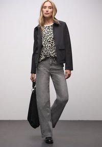 Czarna dopasowana kurtka, top w panterkę, szare szerokie dżinsy i czarne botki, trzyma czarną torbę typu tote. Gładkie tekstury i współczesny design.