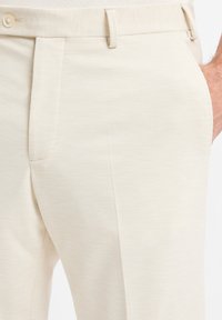 Beige Anzughose aus glattem Stoff mit Knopfverschluss, seitlichen Taschen und einem klaren, minimalistischen Design.