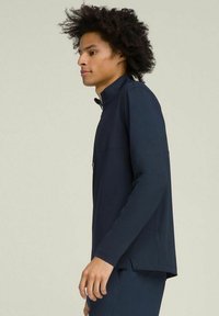 Maglia a maniche lunghe blu navy con colletto alto, texture liscia e zip frontale. Presenta spacchi laterali e una silhouette aderente.