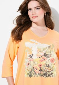 Orange, V-Ausschnitt-Shirt mit Dreiviertelärmeln, das einen Blumenprint mit Mohnblumen und einem Vogel in sanften Pastelltönen zeigt, aus leichtem Material gefertigt.