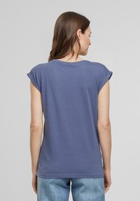 Blaue Baumwoll-T-Shirt mit umgeschlagenen Kurzärmeln, rundem Halsausschnitt und geradem Schnitt. Getragen mit hellblauen Jeans.