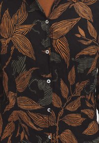 Black shirt with orange and green leaf pattern. Features button closure and textured fabric. Dominant colors are black, orange, and green.