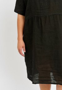 Schwarzes Leinenkleid mit kurzen Ärmeln, das eine geraffte Taille und eine lockere Passform aufweist und eine leicht zerknitterte Textur zeigt.
