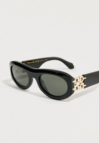 Μαύρα πλαστικά γυαλιά ηλίου με σκουρόχρωμους φακούς, καμπυλωτά πλαίσια και διακοσμητικό στοιχείο σε χρυσό τόνο στις ναούς. Σχεδιασμός επίπεδος και ευρύς.