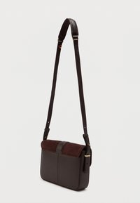 Ciemnobrązowa torba crossbody z teksturowanym skórzanym korpusem i miękkim zamszowym klapą. Smukły pasek i złote akcenty dopełniają design.