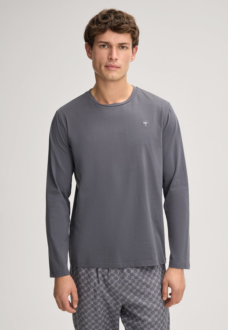 Langærmet grå skjorte lavet af blødt stof, med en rund halsudskæring og et lille, simpelt logo på brystet. Kombineret med mønstrede bukser.