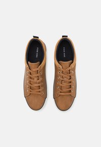 Brown sneakers with a textured suede finish, round toe, contrasting laces, and a sleek white outsole. Black interior with logo.