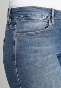 Modré džíny z denimu s přiléhavým střihem, středním pasem, pěti kapsami, jemným zesvětlením a měděnými kovovými detaily.