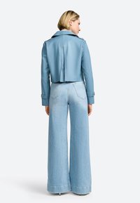 Giacca di pelle azzurro chiaro tagliata con uno spacco sul retro, abbinata a jeans in denim chiaro a vita alta e gamba larga.