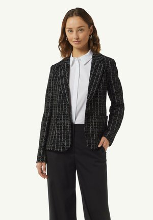 Zwart-wit geruite blazer van een gestructureerde stof, met gesneden revers en een getailleerde pasvorm, gecombineerd met een wit overhemd met boord en zwarte broek.
