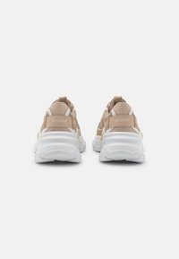Scarpe sportive beige con suole bianche, texture in rete, tacco imbottito e accenti gialli notevoli; marchiate "BOGNER" sul retro.