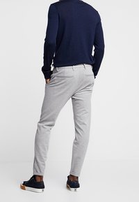 Szare zwężane spodnie z tylnymi kieszeniami, noszone z ciemnym swetrem i czarnymi sneakersami. Gładki materiał, elastyczna talia i regulowane dopasowanie.