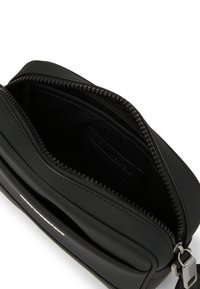 Fekete szintetikus keresztbody táska cipzáros záródással, sima külső felülettel, puha tapintással és egy kis belső címkével. Kompakt kialakítás.