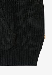 Gros plan du poignet d'un pull noir en maille avec un motif côtelé texturé et une petite étiquette en tissu sur le côté.
