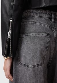 Chaqueta de cuero negro con detalles de cremallera plateada y tela de mezclilla gris con textura desgastada y costuras de los bolsillos traseros visibles.